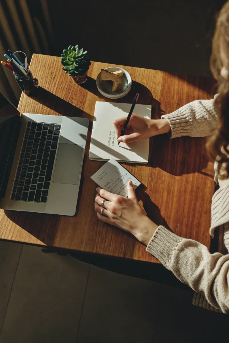 Writing notes at a desk beside a laptop